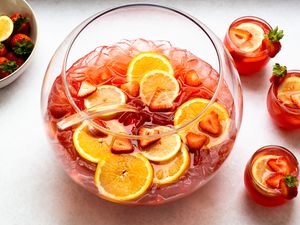 A bowl full of strawberry Champagne punch with three glasses full of the drink