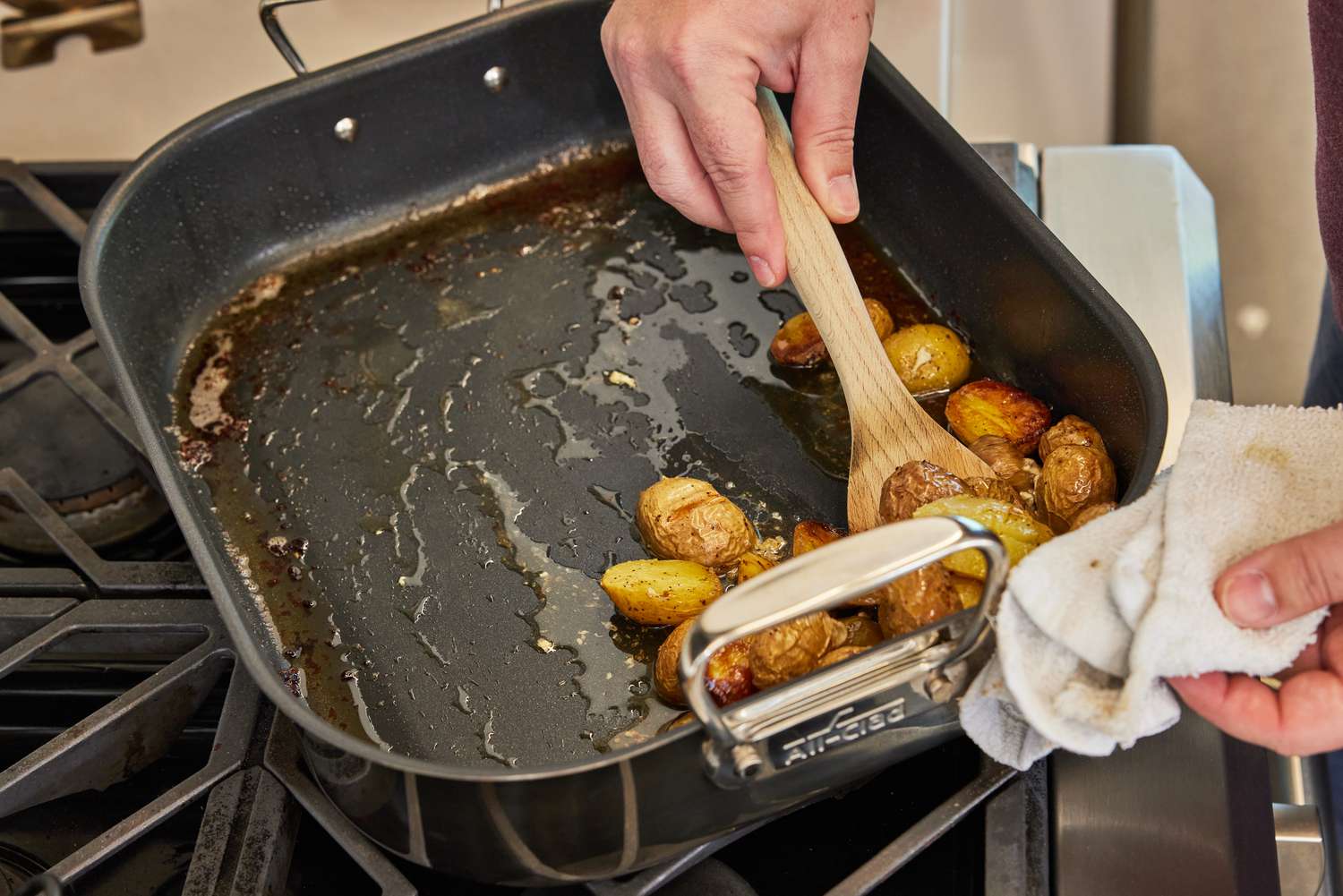 Hand scooping potatoes out of the All-Clad Stainless Steel Nonstick Roasting Pan With Rack