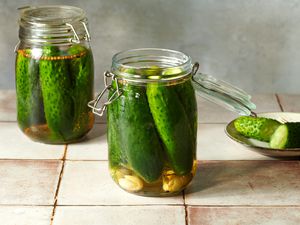 Two jars of half sour deli-style pickles, with a pickle cut in half on a small plate 