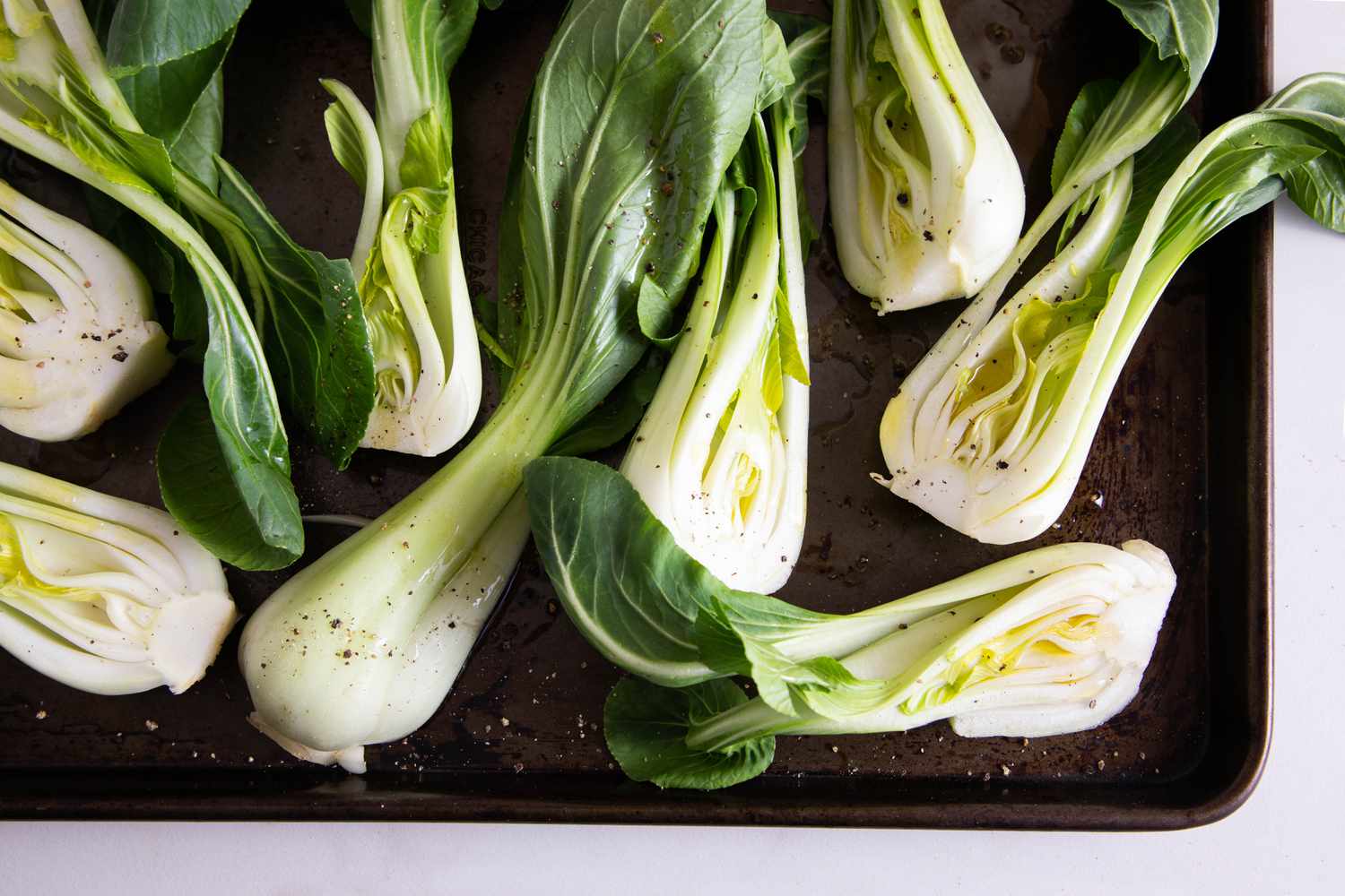 Bok choy sliced in halves and seasoned with olive oil and black pepper on a rimmed baking sheet