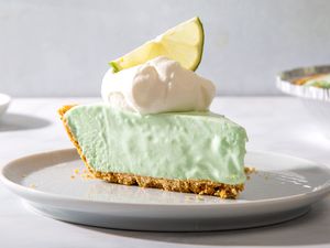 A plated slice of Lime Jello Cool Whip Pie topped with whipped cream and a slice of lime