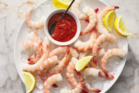 A large plate of shrimp cocktail, served on ice with lemon wedges and cocktail sauce