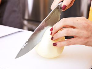 Hand holding Wusthof Classic IKON 8-inch Knife while slicing white onion