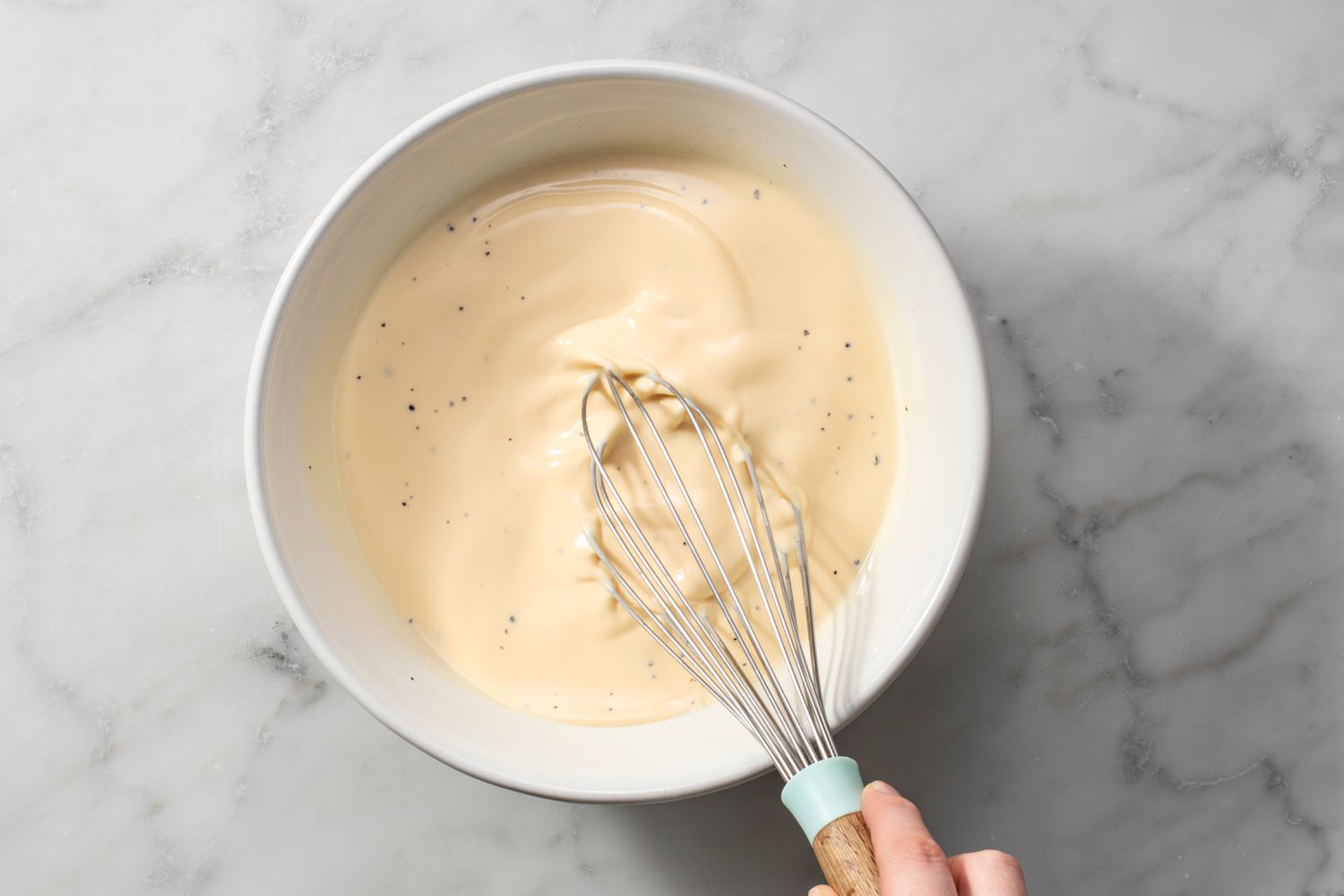 A hand whisking eggs, cream, salt, and pepper in a bowl