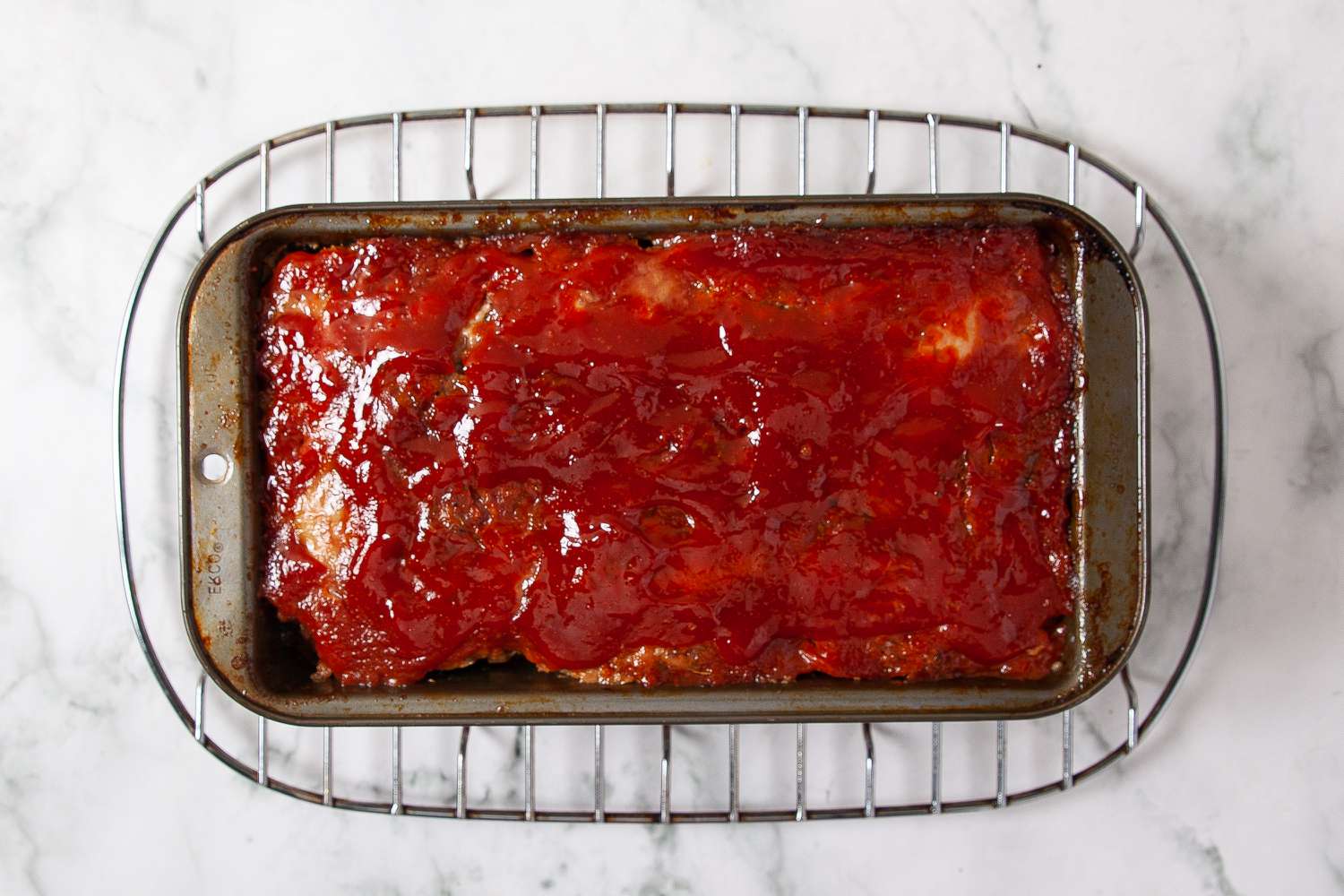 Meatloaf with sausage and ketchup glaze in loaf pan on a wire rack