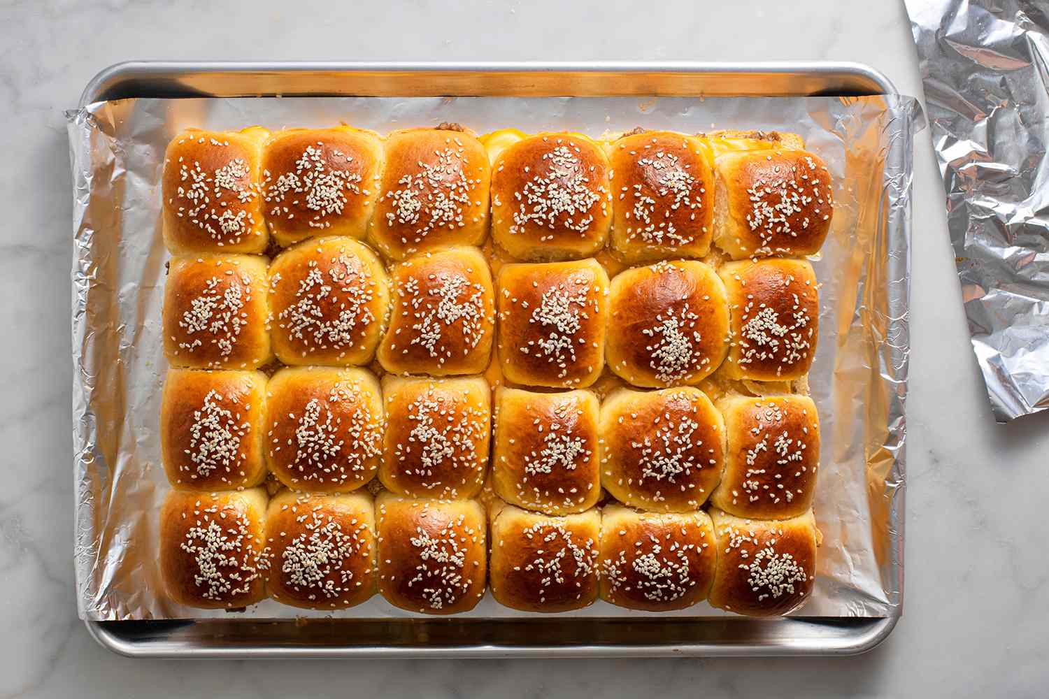 A baking sheet of baked sliders with aluminum foil 