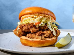 A crispy fried mushroom sandwich with cabbage slaw and mayo, served with a dill pickle spear and a glass of beer