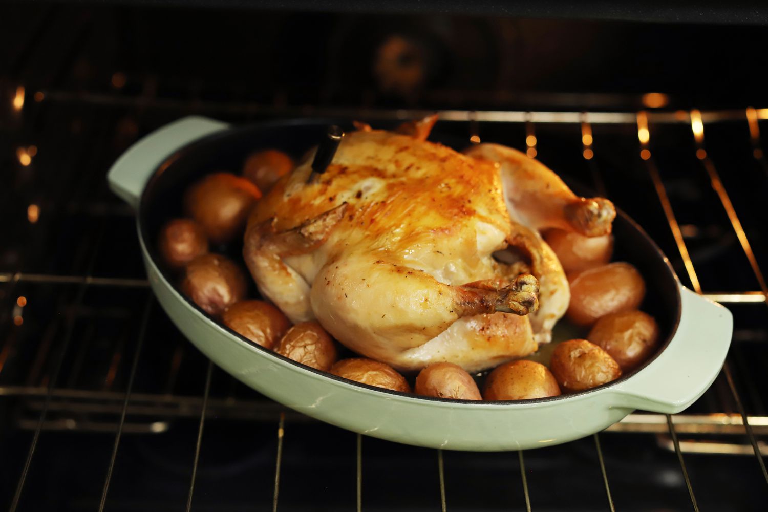 Chicken roasting on small potatoes in the KitchenAid oval cast iron roasting pan