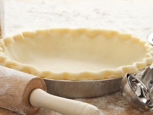 An empty pie crust with rolling pin, measuring spoons.