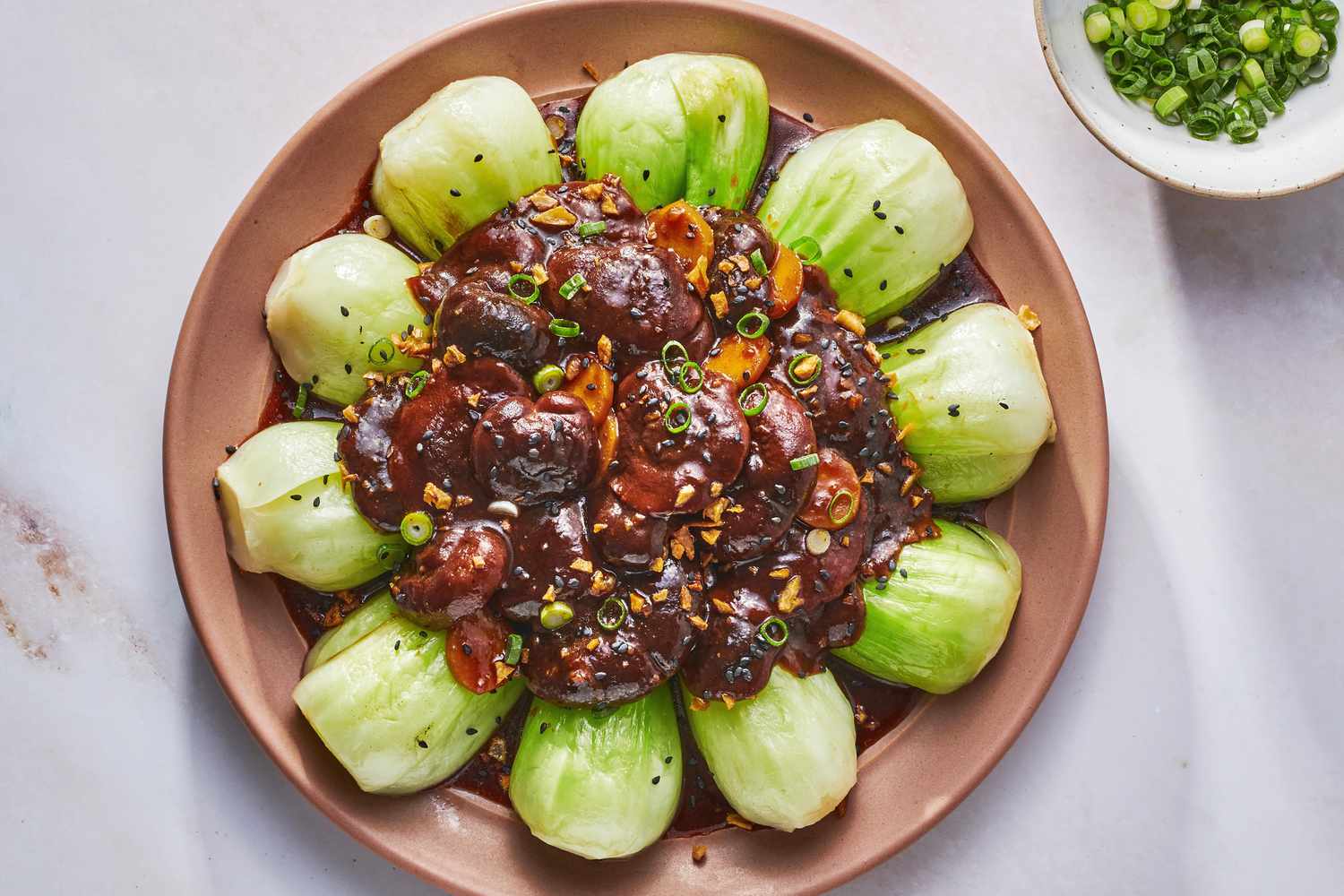 A large plate of braised shiitake mushrooms served on top of boy choy, and a small bowl of sliced scallions