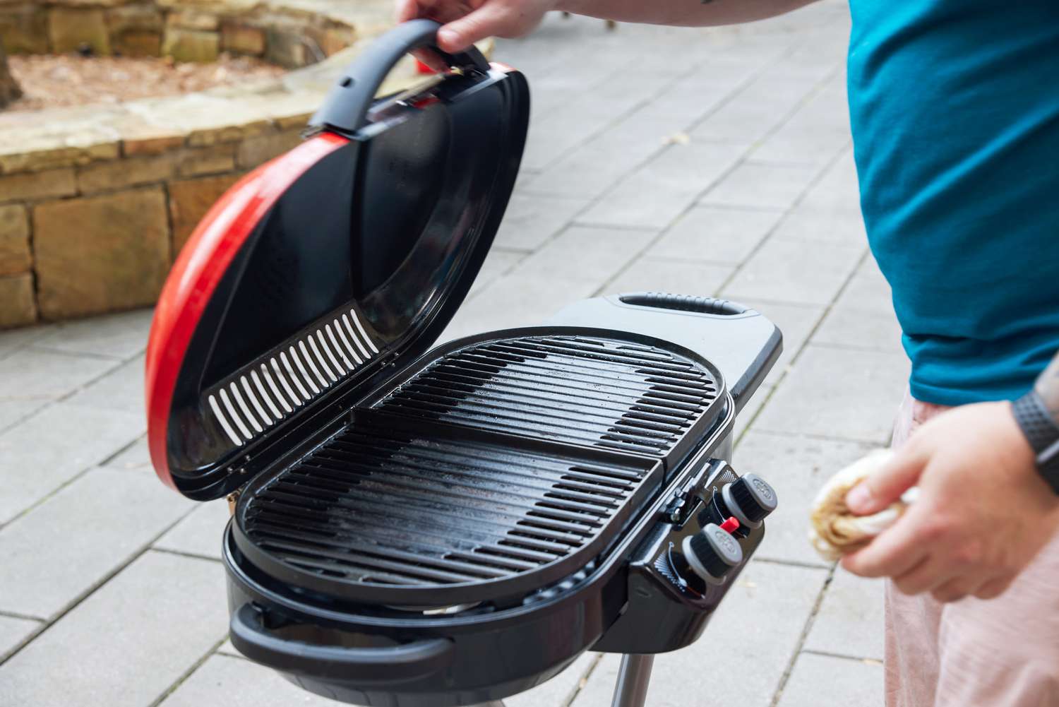 A person lifts the lid on the Coleman RoadTrip 225 Portable Tabletop Propane Grill