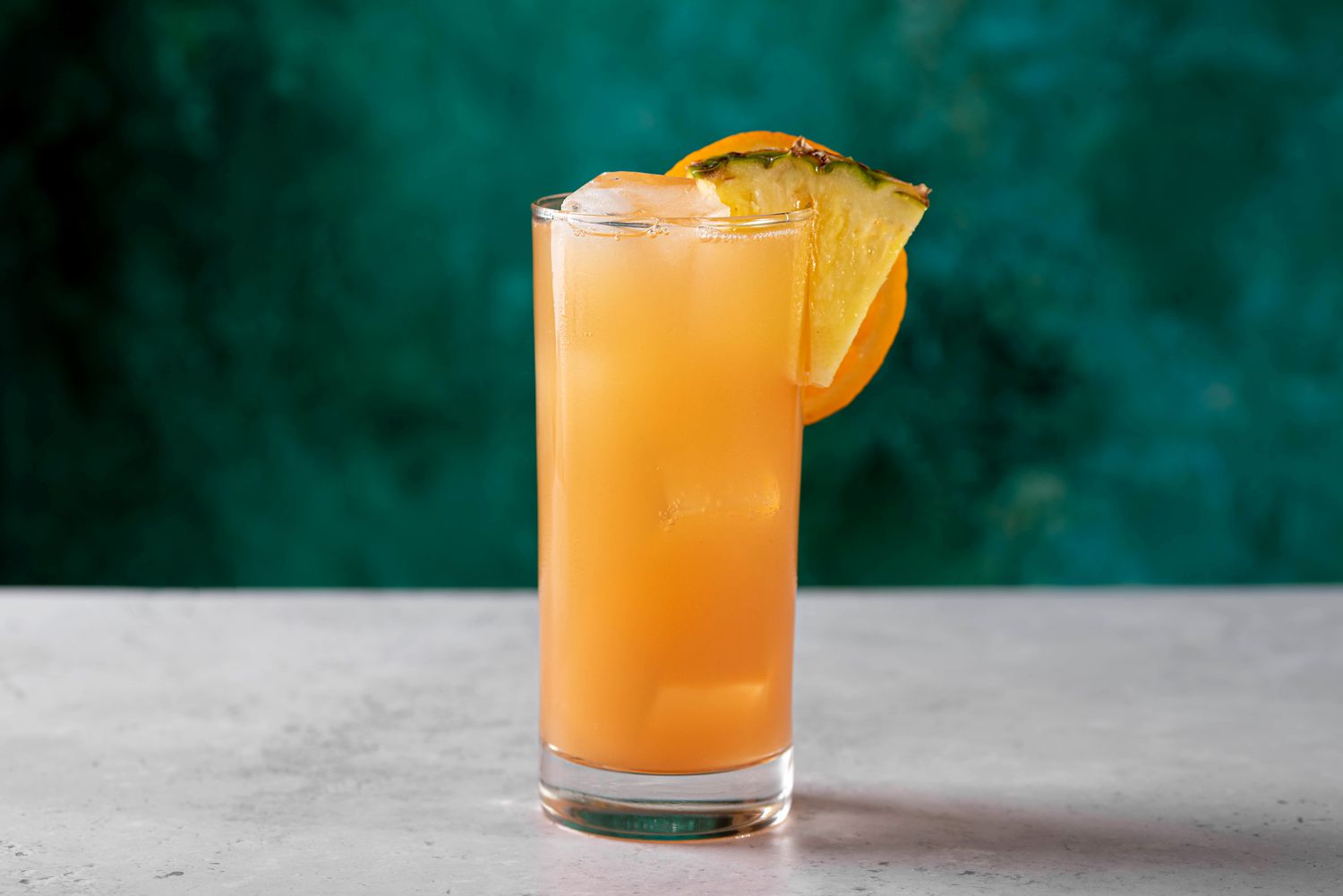 Bright-orange Cinderella mocktail drink back drop with sliced orange garnish against a blue-green 