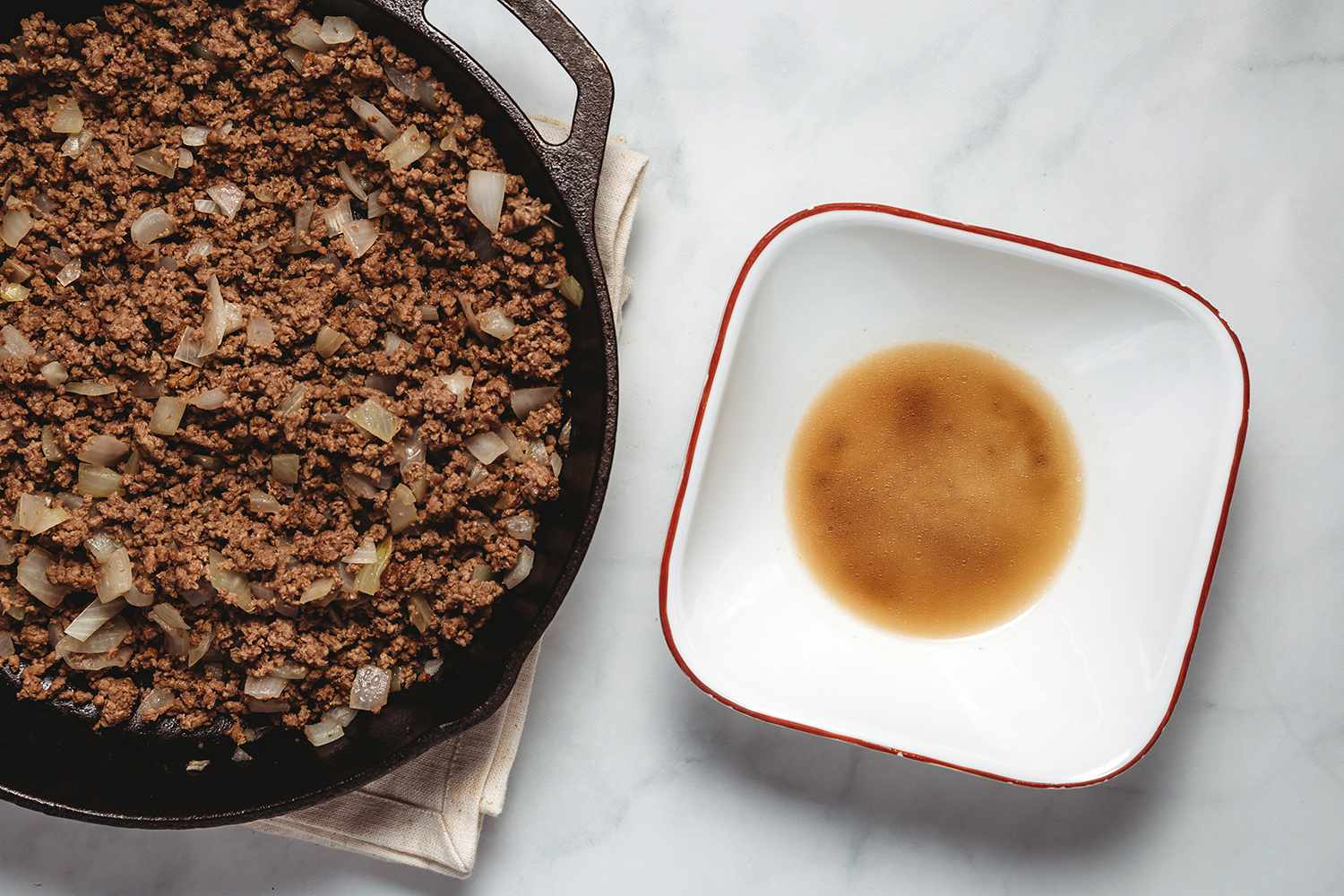 Beef and onions in a cast iron and drained beef fat in a bowl 