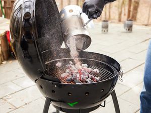 Person dumping burning charcoal from chimney starter onto Char-Broil TRU-Infrared Kettleman Charcoal Grill