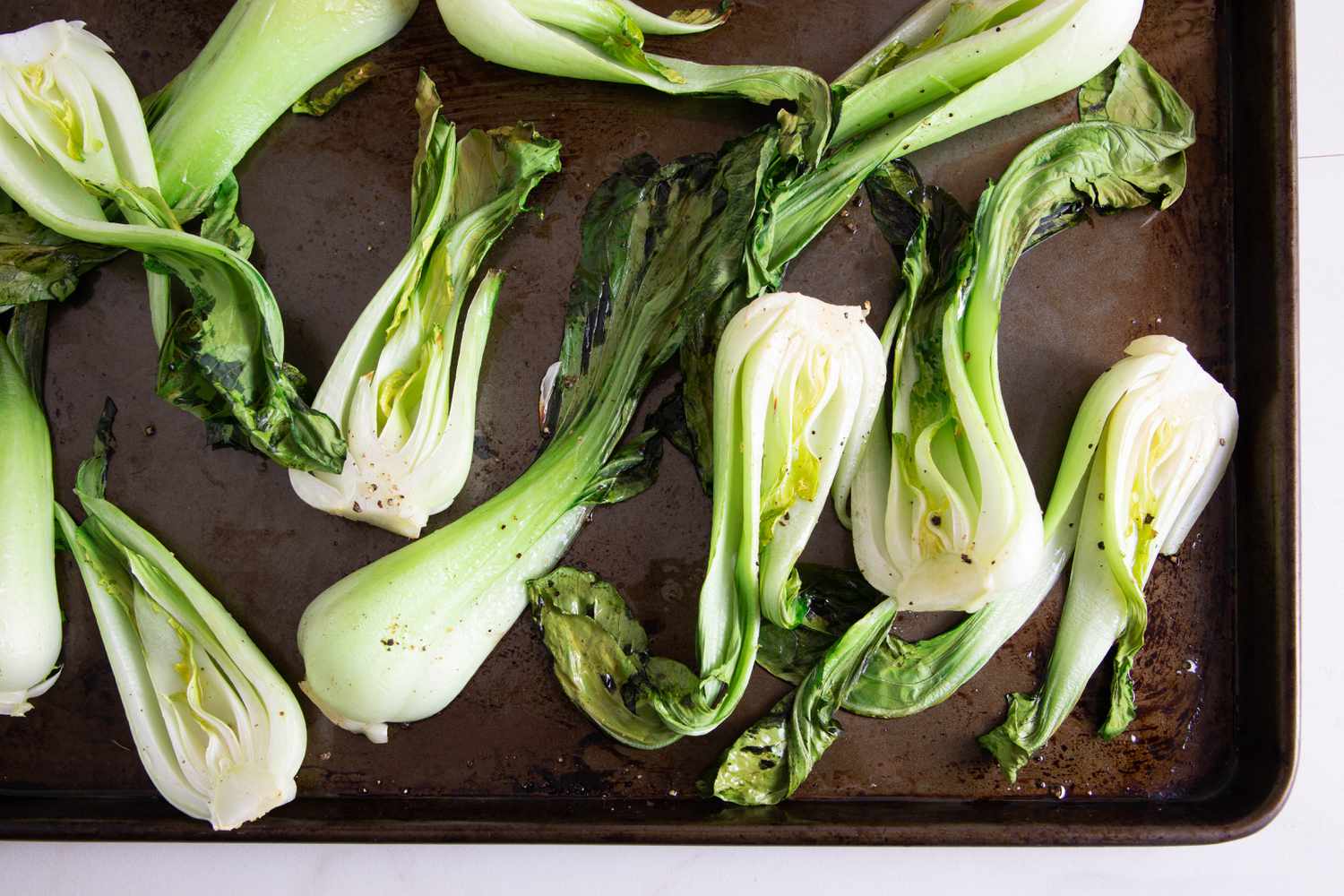 Baked bok choy, its ends frizzled, on a baking sheet 