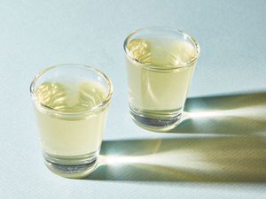 Two green tea shots on a pale green surface