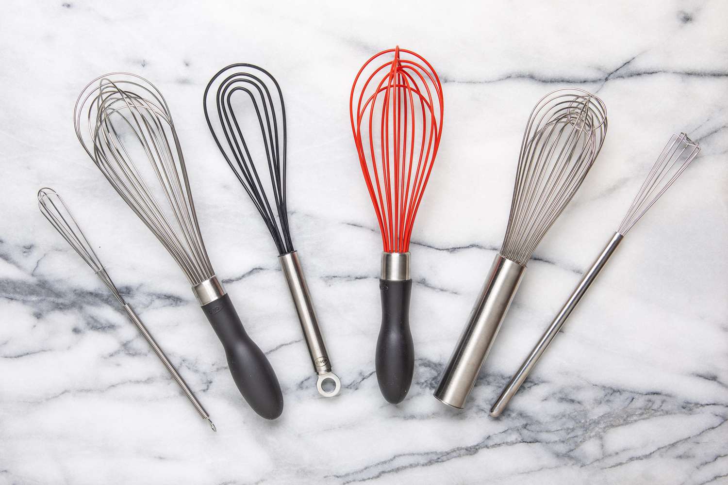 A variety of whisks on a marble surface