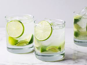 Two caipirinha cocktails in clear glasses garnished with lime