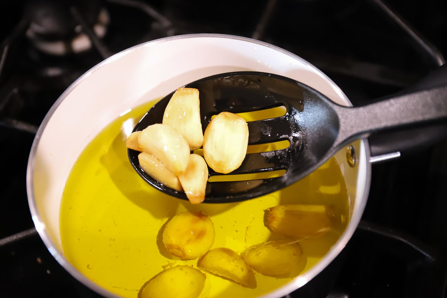 Closeup of a slotted spoon lifting garlic from a pot from the T-fal Initiatives Ceramic Nonstick Cookware Set