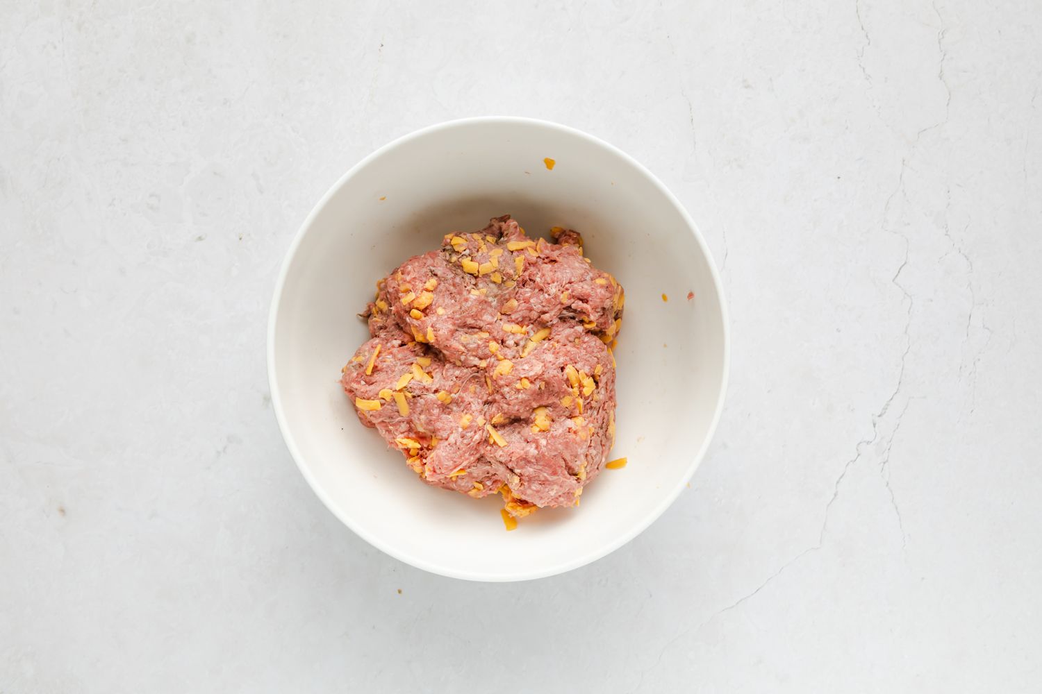burger meat mixed with some shredded cheese in a bowl 