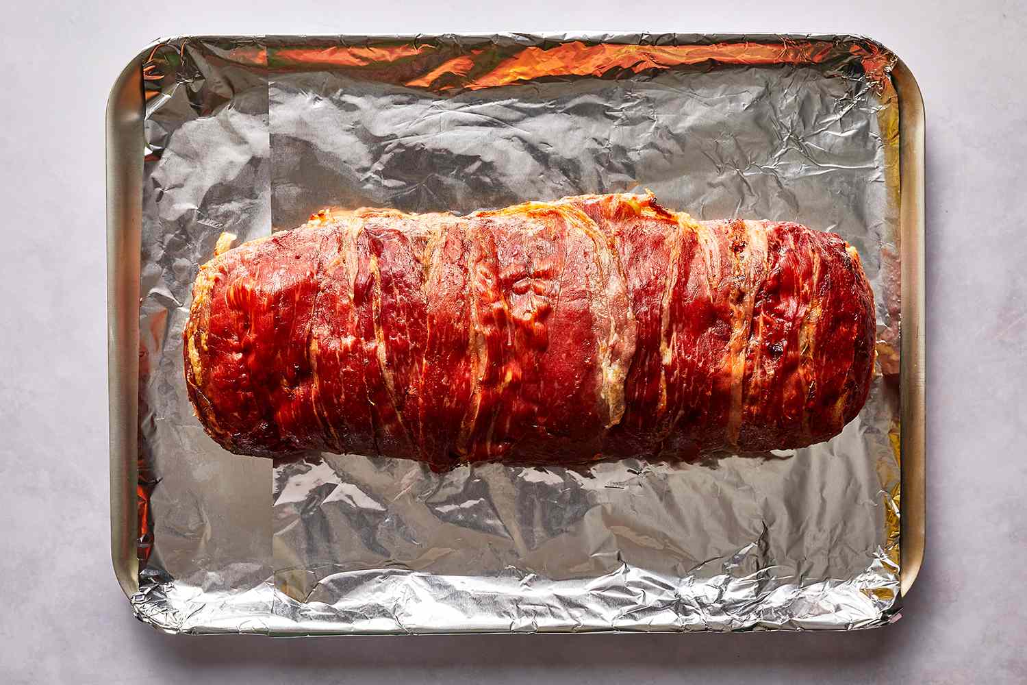 Baked Prosciutto-Wrapped Stuffed Meatloaf on an aluminum foil lined baking sheet 