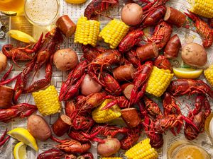 Boiled crawfish, sausage, potatoes, and corn laid out in a newspaper, served with lemon wedges and beer
