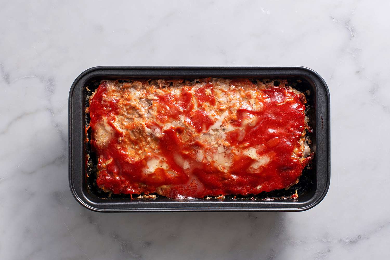 Baked meatloaf with lightly browned top, pulling away from the sides of the loaf pan