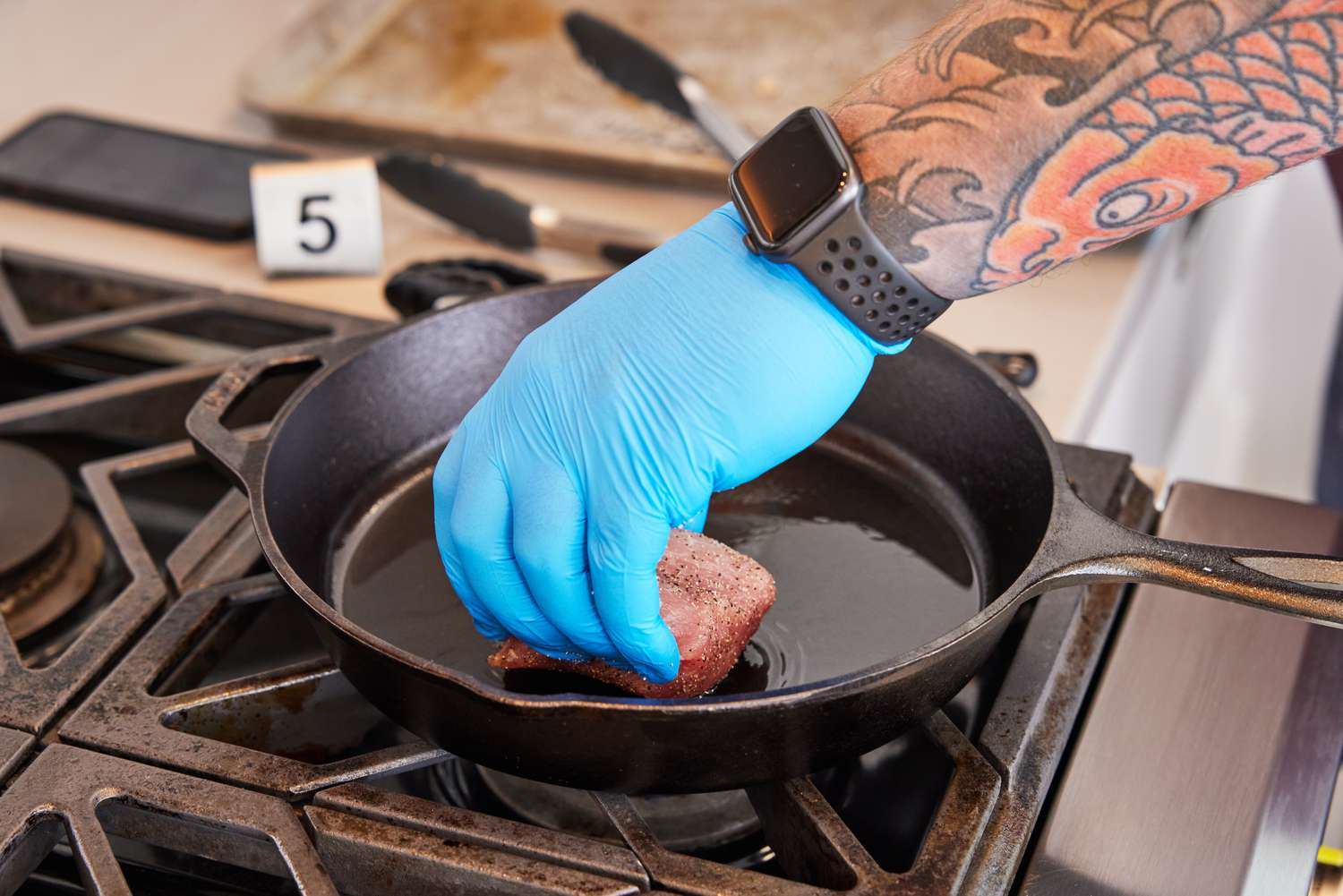 Hand placing a piece of meat into a Lodge Pre-Seasoned Cast Iron on a stovetop