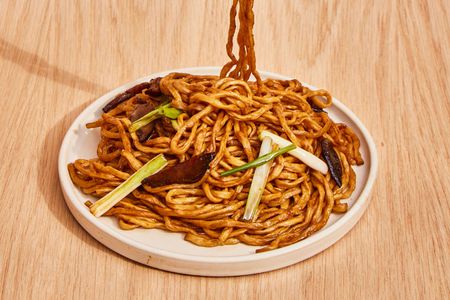 A plate loaded up with longevity noodles, showing mushrooms and scallions mingled with the glazed noodles