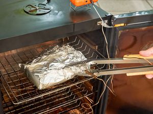 A person removes meat from the Bradley Smoker 4-Rack Outdoor Electric Smoker, Natural Draft Smoker (BS611)