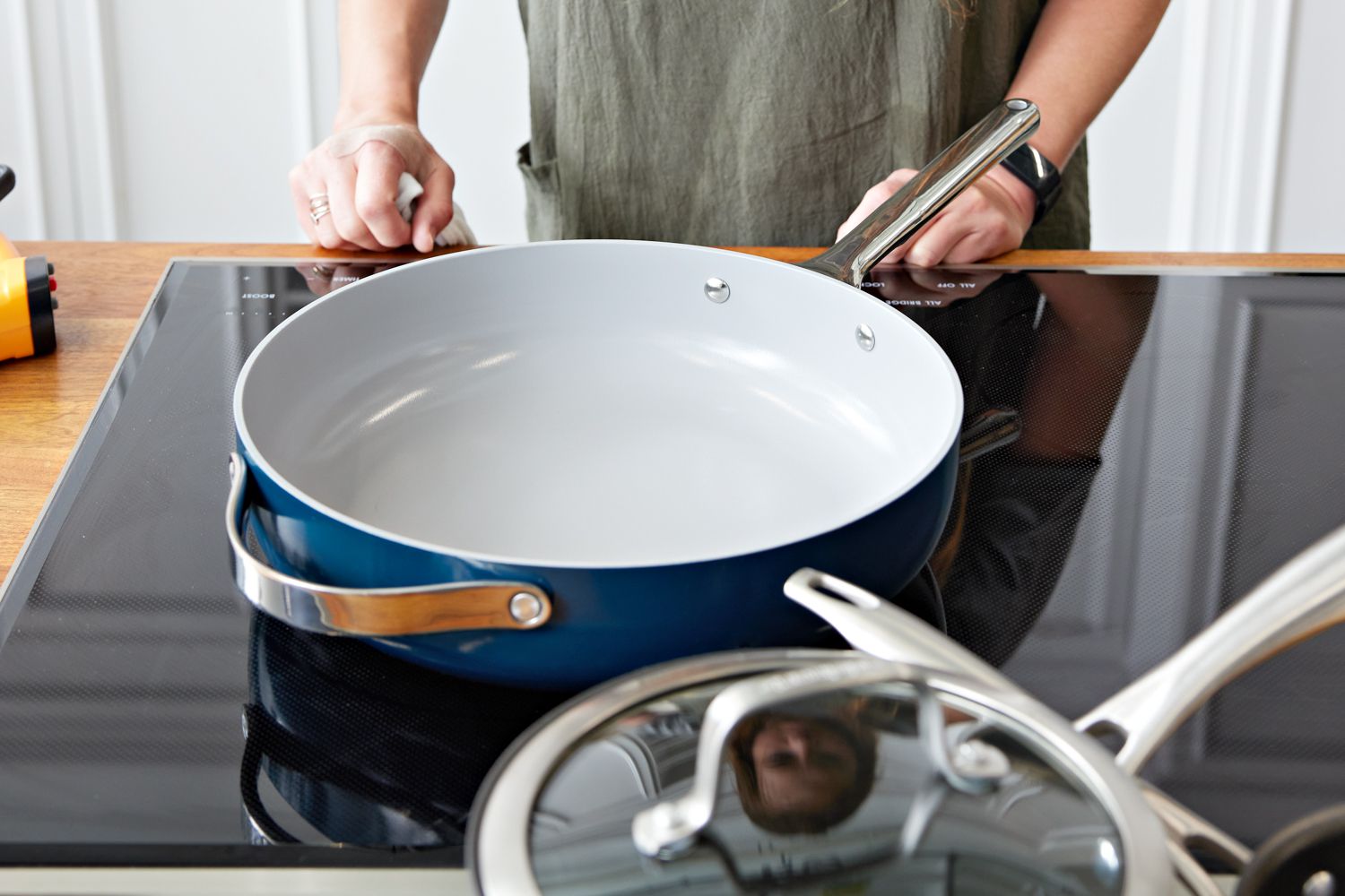 Person standing behind a Caraway Cookware Set saute pan displayed on glass stovetop