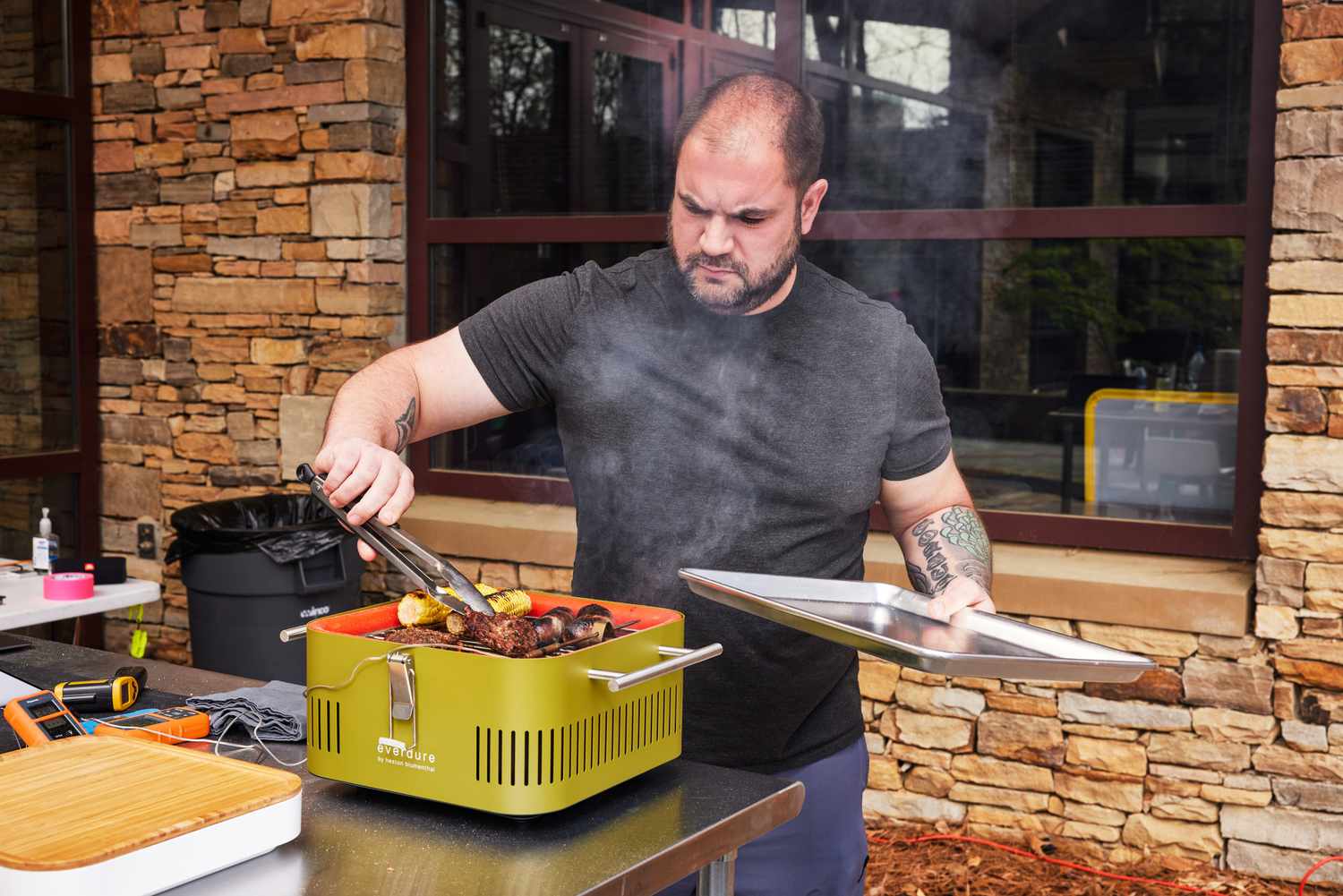 Man removing meat with tongs from Everdure Cube Portable Charcoal Grill