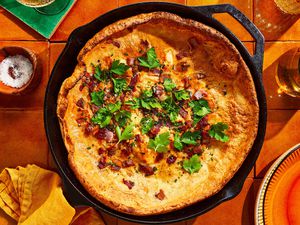 A savory bacon and cheese dutch baby served in a cast iron pan, garnished with parsley 