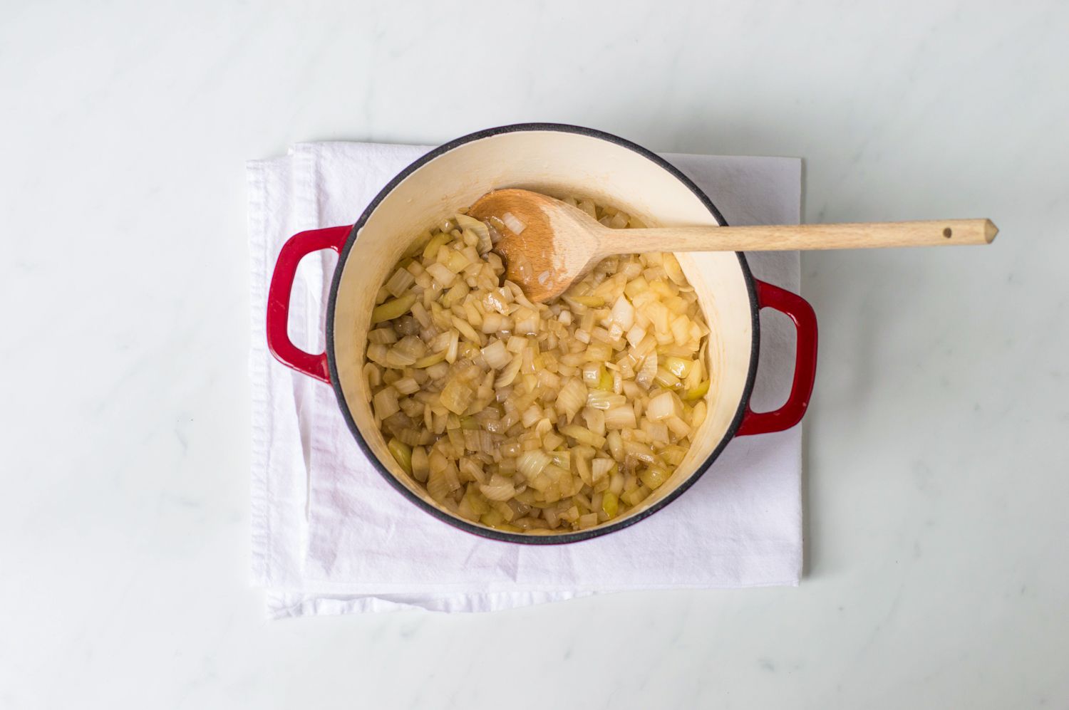 Beer added to onions in a Dutch oven with a wooden spoon