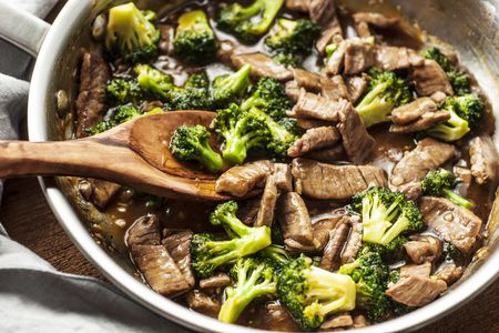 Beef and broccoli stir fry in a skillet with a wooden spoon