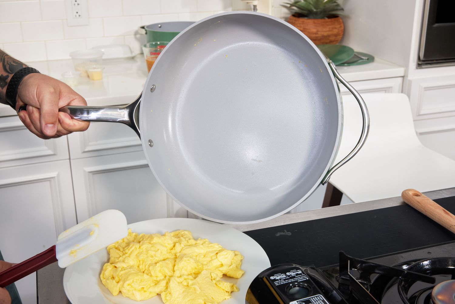 Hand holding handle of Caraway Cookware Set fry pan over plate of scrambled eggs