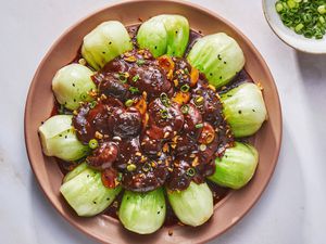 A large plate of braised shiitake mushrooms served on top of boy choy, and a small bowl of sliced scallions