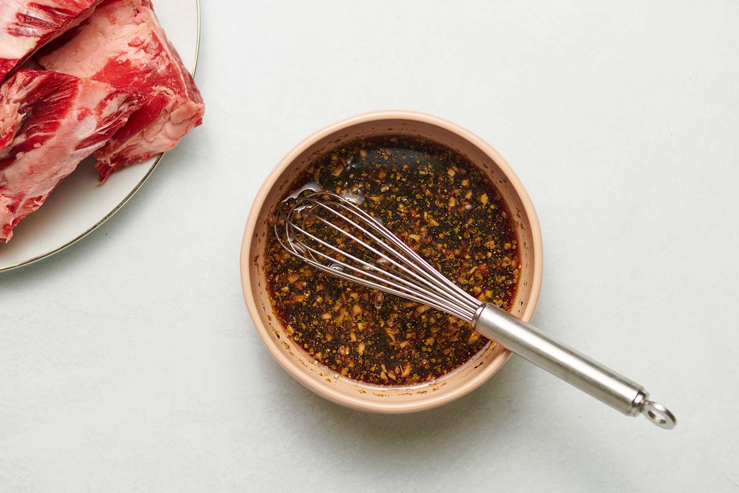 Marinade in a bowl with a metal whisk and beef ribs on a plate 