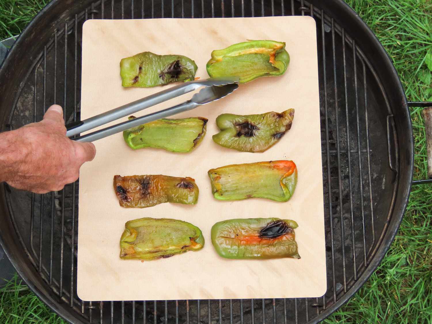 A tester flips green peppers on a Yoshi copper grilling mat over a charcoal grill.