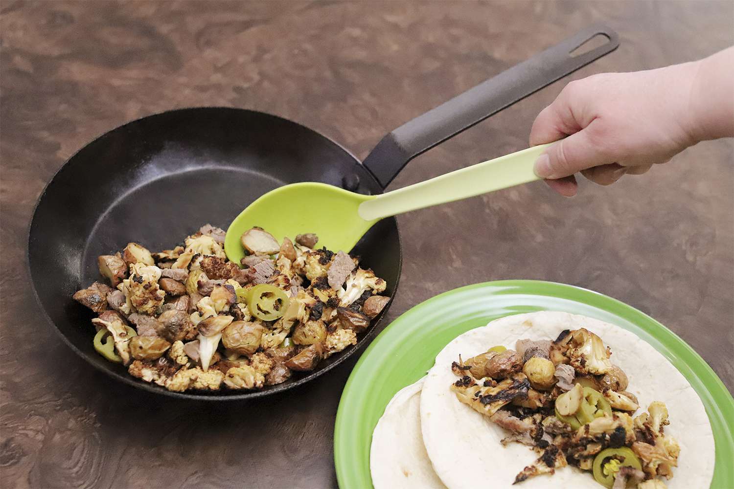 Hand using green spoon to scoop meat from the Lodge Seasoned Carbon Steel Skillet and tacos on a green plate