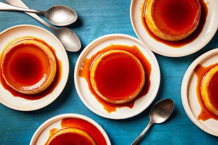 Five individual servings of mango flan with spoons on a blue surface