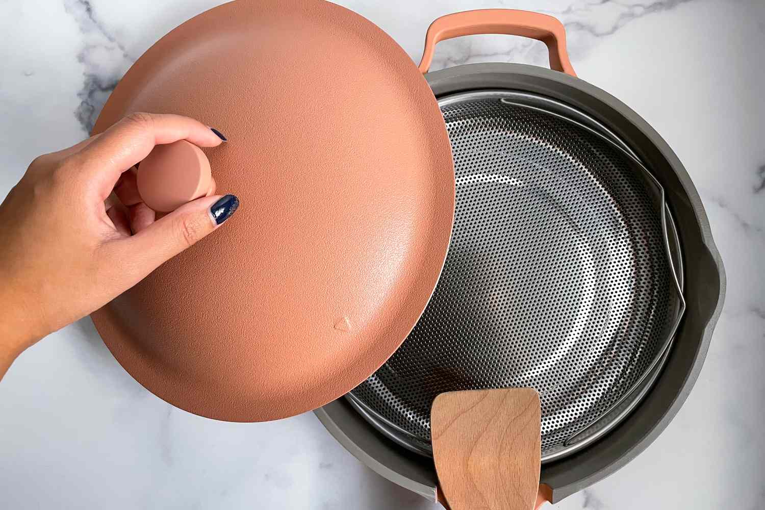 Hand taking the lid off an empty Always Pan, while on a marble counter