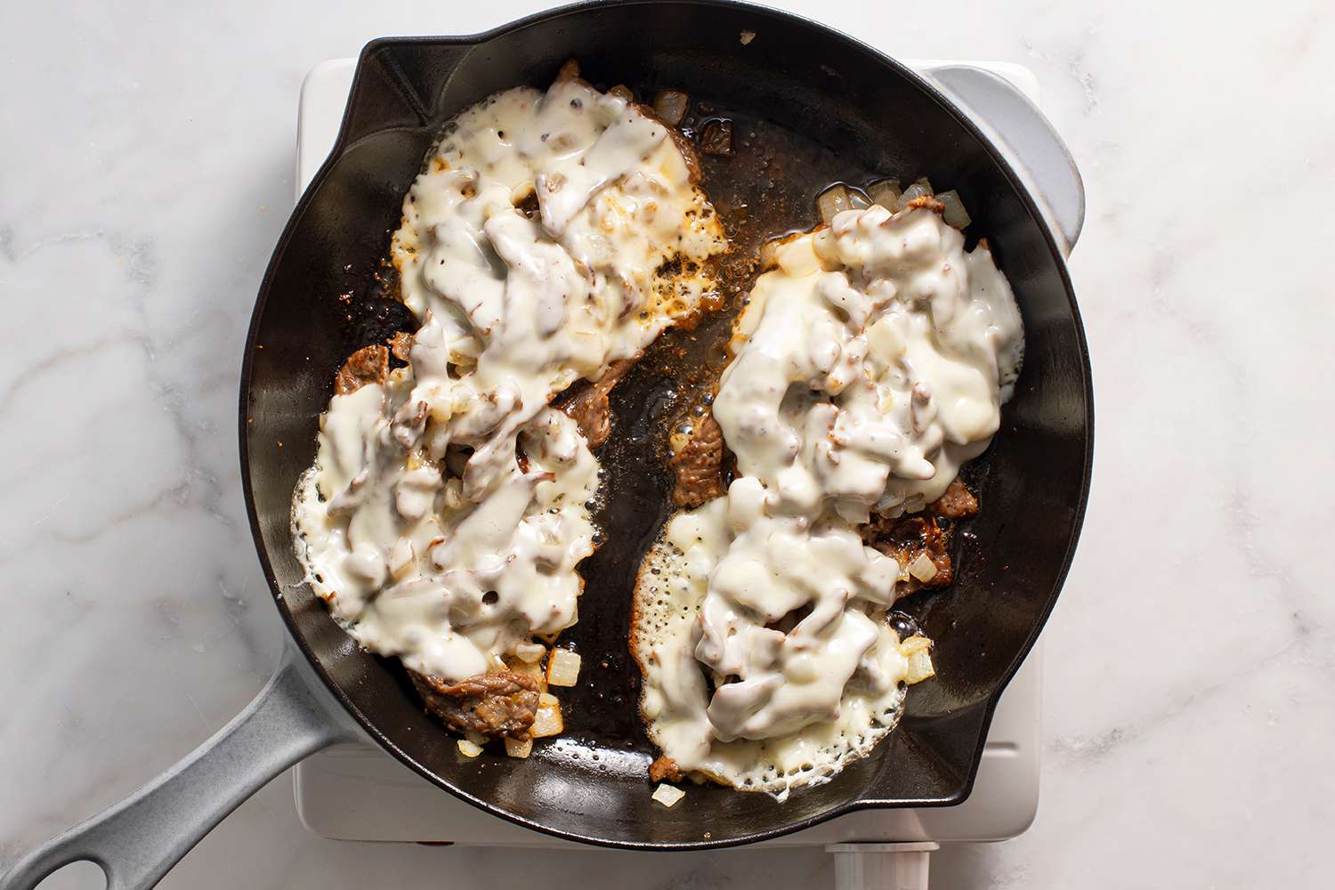 Two portions of steak and onions covered with melted cheese in a pan