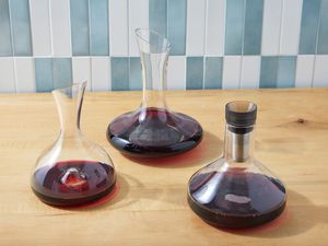 Three wine decanters filled with red wine, on a wooden counter