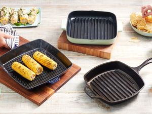 Three grill pans displayed on a wooden table with grilled corn and tortilla trips