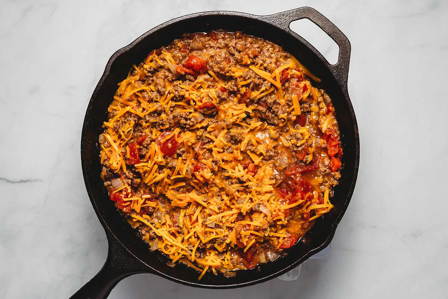 Shredded cheese added to the beef mixture in the cast iron pan 