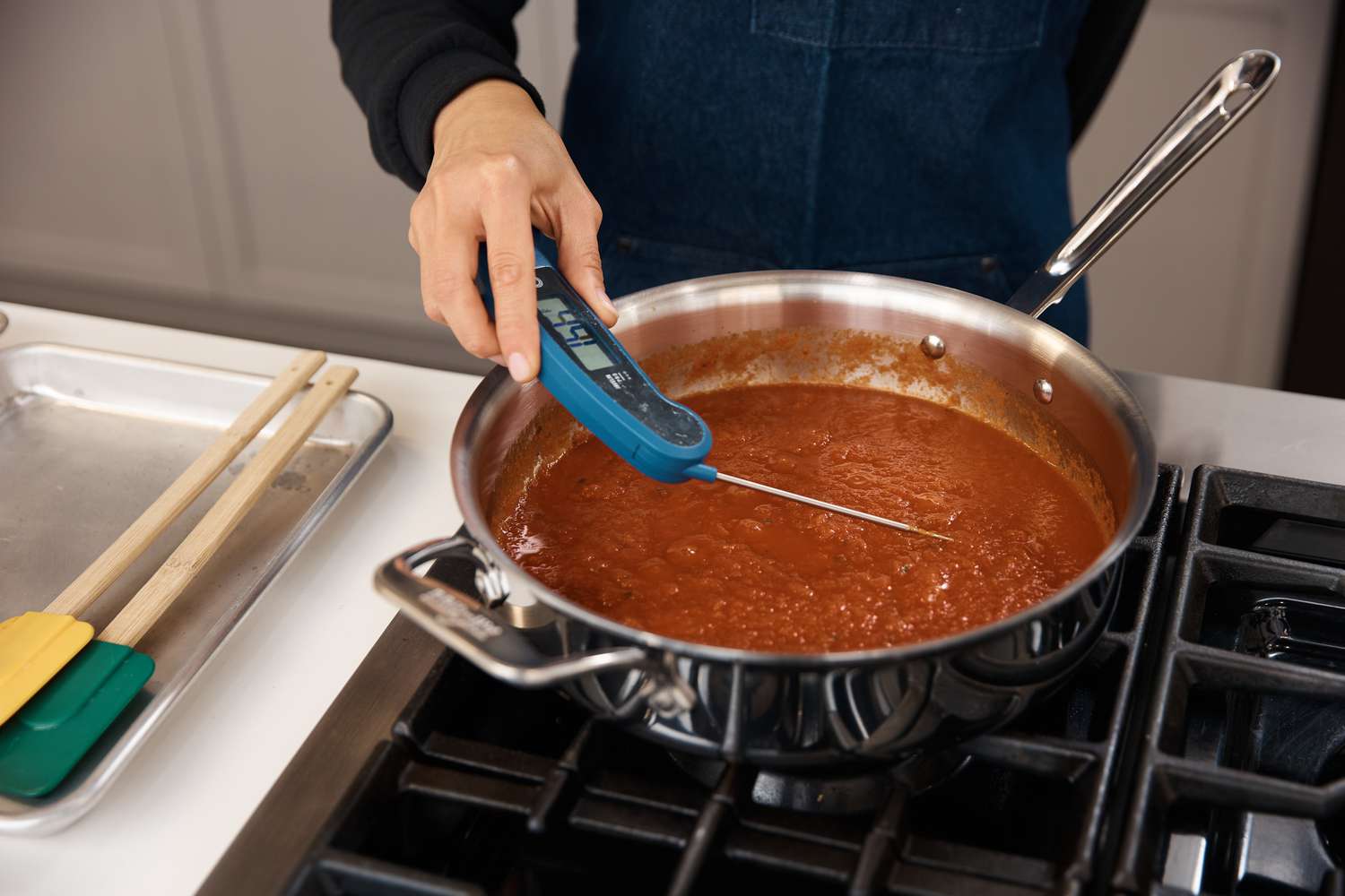 Person checking the temperature of sauce in pan from All-Clad D5 Stainless Brushed 5-Ply Bonded 10-Piece Cookware Set