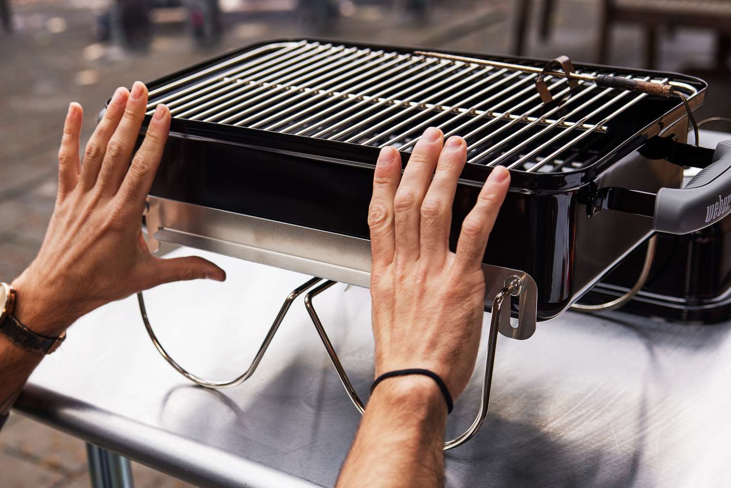 Hands touching the Weber Go-Anywhere Charcoal Grill displayed on a table 