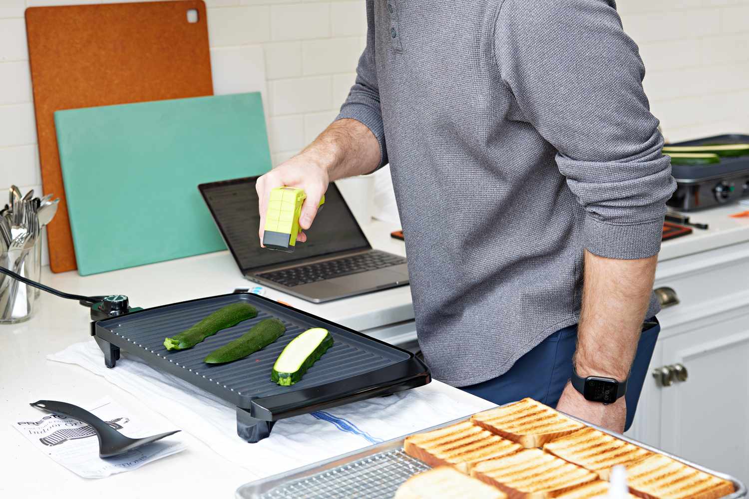 Man measuring the temperature of the Presto 09020 Cool Touch Electric Indoor Grill that's cooking zucchini slices 