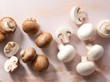 Brown and white button mushrooms on a light pink surface